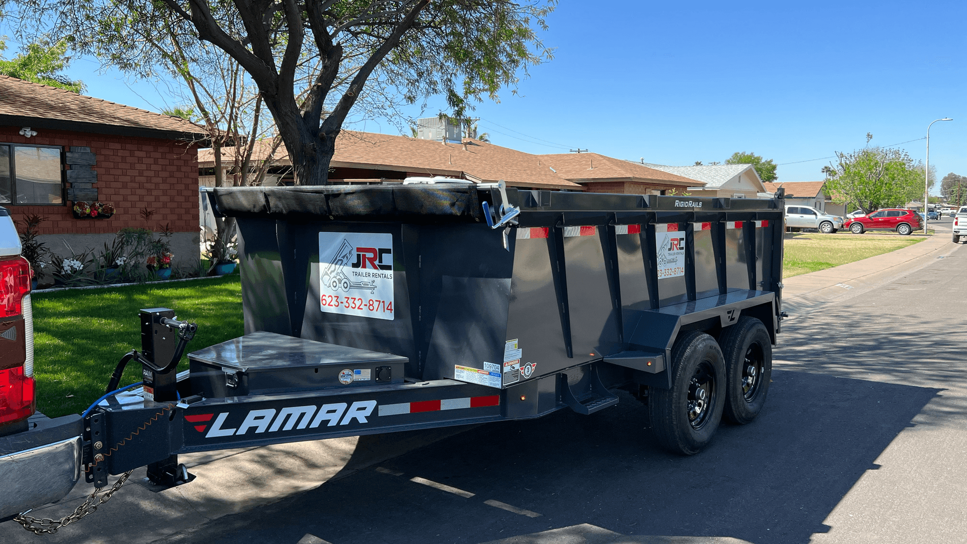 Large black trailer parked on a residential street with trees and houses in the background.